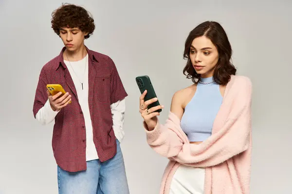 Casal jovem absorvido em seus telefones, irradiando moda em um ambiente de estúdio brilhante. — Fotografia de Stock