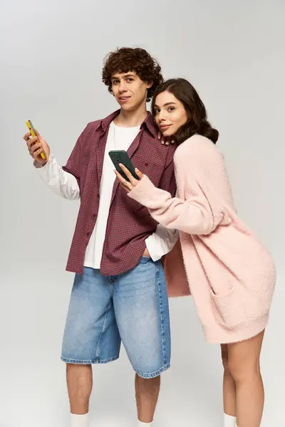 Stylish young man and woman pose together, smiling and enjoying their phones in a light setting. — Stock Photo