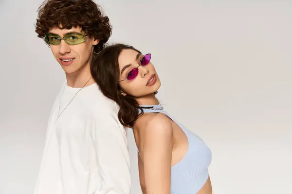 A couple poses back to back, showing off their stylish sunglasses in a bright studio. — Stock Photo