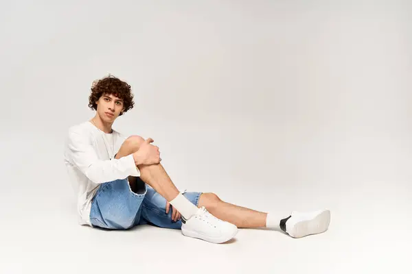 Curly haired man in fashionable attire on serene white backdrop. — Stock Photo