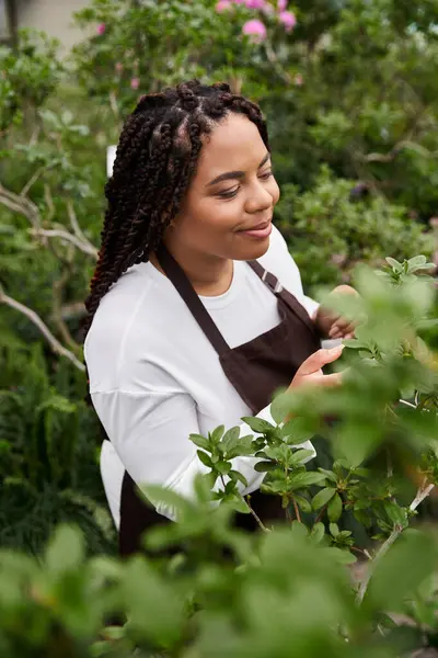 Uma mulher afro-americana gosta de cuidar de plantas vibrantes em uma estufa ensolarada. — Fotografia de Stock