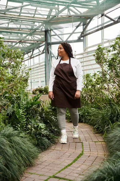 Uma mulher afro-americana que tende a exuberar plantas em um ambiente de estufa sereno. — Fotografia de Stock