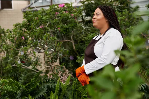 An African American woman with braids enjoys her time tending to lush plants in a sunny greenhouse. — Stock Photo
