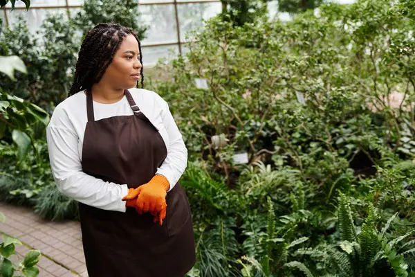 A dedicated gardener enjoys the lush greenery in a vibrant greenhouse filled with plants. — Stock Photo