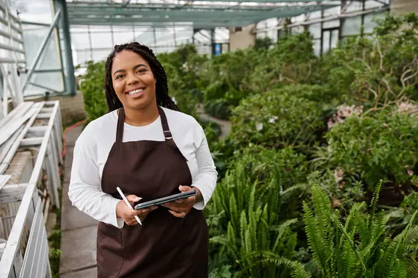 A dedicated gardener with braids enjoys her time tending to lush greenery in a greenhouse. — Stock Photo