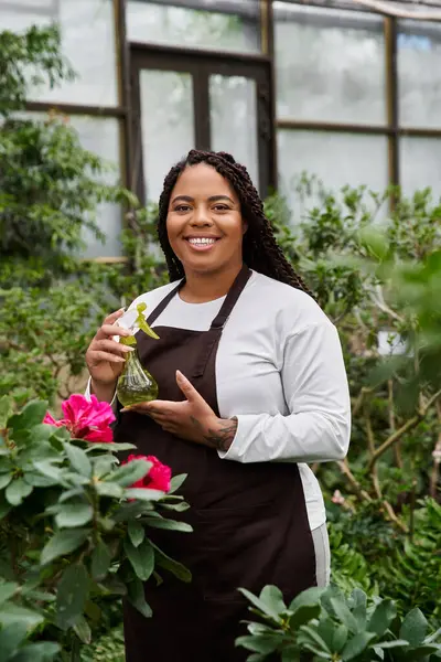 An African American woman with braids stands confidently in a greenhouse, caring for plants. — Stock Photo