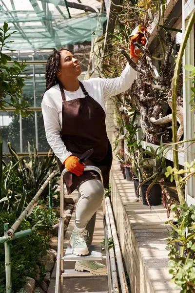 Uma mulher afro-americana tende a plantar em uma estufa brilhante, sentindo-se feliz e conectada. — Fotografia de Stock