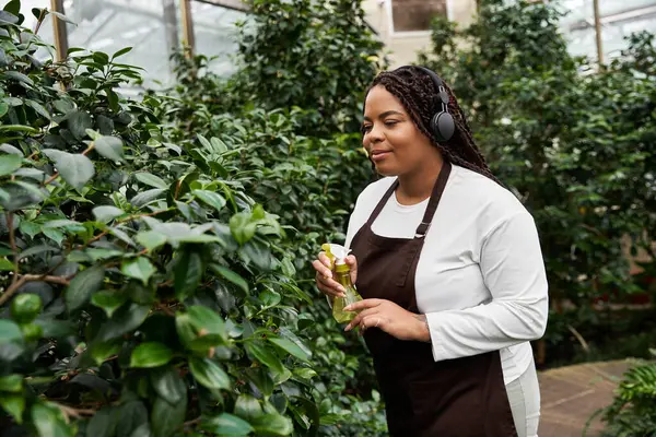 A happy gardener tends to lush plants in a greenhouse, enjoying her nurturing environment. — Stock Photo