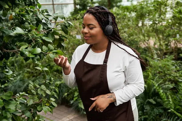 An African American woman with braids tends to plants in a lush greenhouse, finding bliss in nature. — Stock Photo