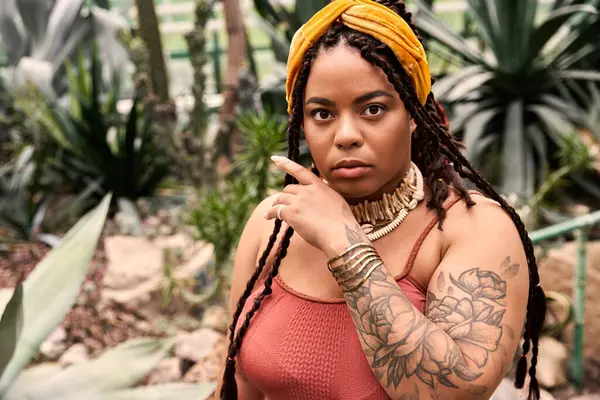 A beautiful Black woman with braids relaxes in a greenhouse filled with lush plants. — Stock Photo