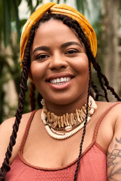 A beautiful African American woman with braids relaxes in a peaceful greenhouse full of plants. — Stock Photo