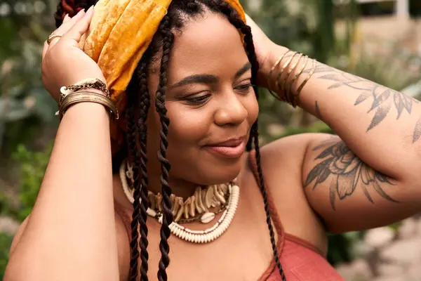 Una alegre mujer negra con trenzas disfruta de su tiempo en un exuberante invernadero lleno de plantas. - foto de stock