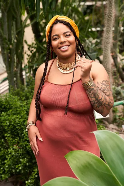 A pretty African American woman with braids enjoys the lush surroundings of a greenhouse. — Stock Photo