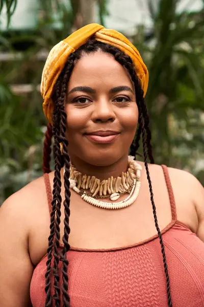 Bright smile of a pretty woman with braids, dressed elegantly, enjoying the greenhouse atmosphere. — Stock Photo