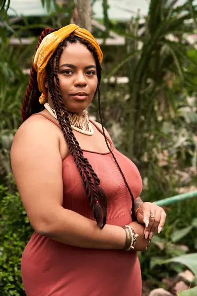 En un invernadero sereno, una mujer radiante con trenzas se levanta con gracia entre las plantas vibrantes. - foto de stock