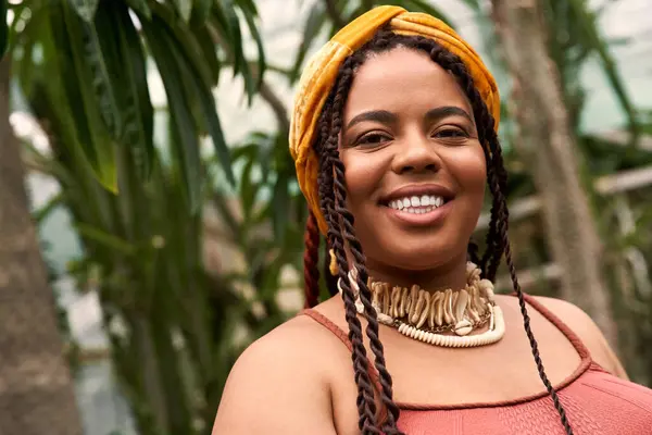A pretty African American woman with braids enjoys a lush greenhouse filled with greenery. — Stock Photo
