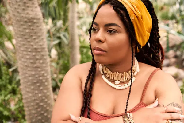 A pretty African American woman with braids stands gracefully in a greenhouse surrounded by plants. — Stock Photo