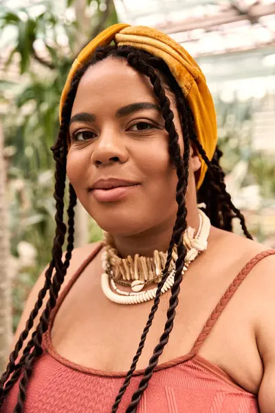 A joyful Black woman with braids relaxes in a tranquil greenhouse filled with greenery. — Stock Photo