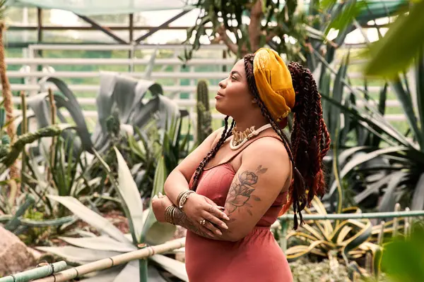 A beautiful African American woman relaxes in a serene greenhouse filled with vibrant plants. — Stock Photo