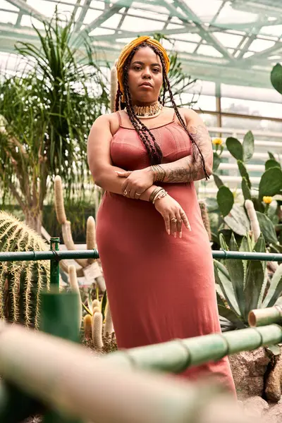 A confident Black woman in a chic dress stands gracefully among lush greenery. — Stock Photo