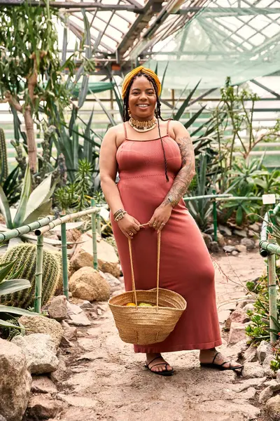 Una gioiosa donna afroamericana si trova tra le piante vibranti in una serena serra, irradiando beatitudine.. — Foto stock