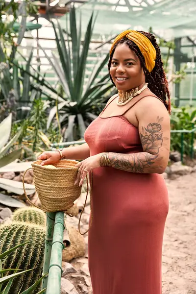 Eine glückliche Frau mit Zöpfen trägt ein schönes Kleid, während sie Pflanzen in einem Gewächshaus genießt. — Stockfoto