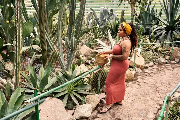 Uma mulher feliz com tranças em um vestido explora uma estufa cheia de plantas diversas. — Fotografia de Stock
