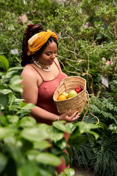 A blissful woman in a dress collects vibrant fruits in a vibrant greenhouse filled with greenery. — Stock Photo