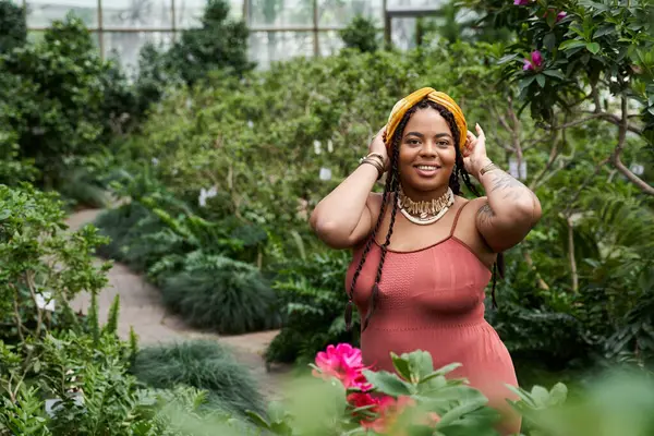 Una bella donna afroamericana in un vestito gode il suo tempo tra le piante tropicali in una serra. — Foto stock