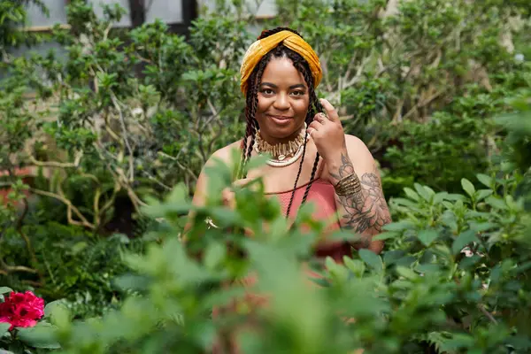 A beautiful Black woman with braids enjoys the lush greenery of a greenhouse. — Stock Photo