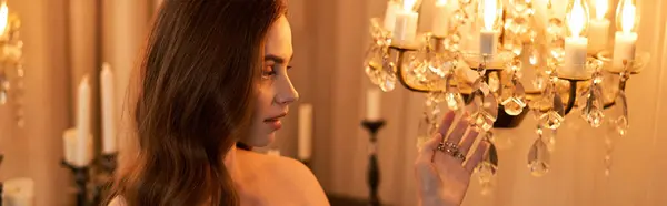 A graceful young woman admires a stunning chandelier while surrounded by soft, warm light, banner — Stock Photo