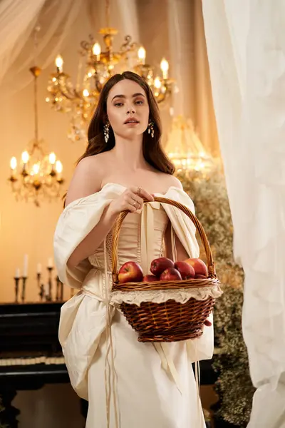 A young woman in vintage attire carries a basket of apples, radiating elegance. — Stock Photo