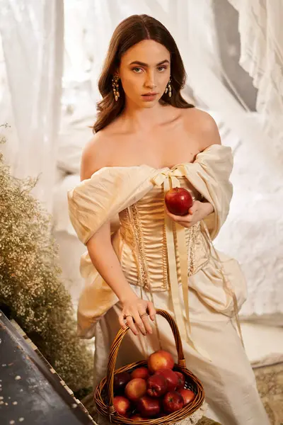 A graceful young woman holds a shiny apple while standing amidst delicate floral decor. — Stock Photo