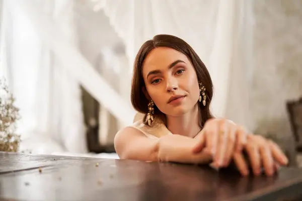 The young woman poses gracefully in a vintage dress, exuding elegance in a soft-lit venue. — Stock Photo