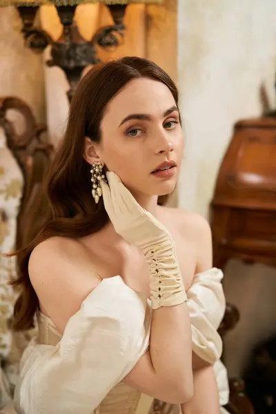 A striking young woman showcases vintage elegance while gracefully posing in a luxurious room. — Stock Photo
