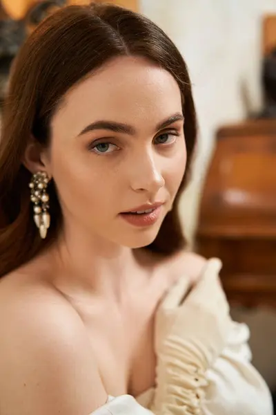 A beautiful young woman in a vintage dress poses gracefully in a stylish indoor space. — Stock Photo