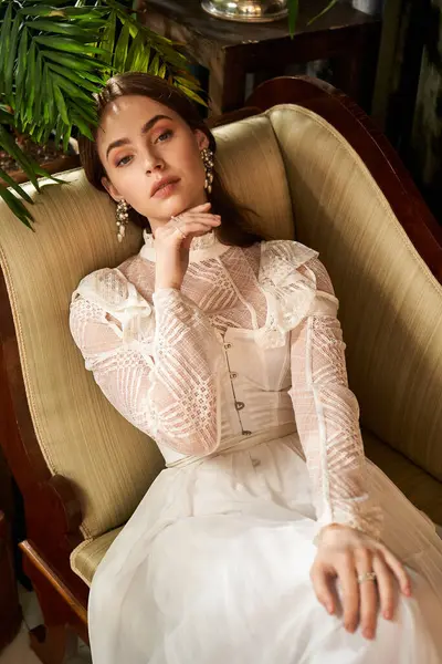 A beautiful young woman in a delicate vintage dress relaxes elegantly on a stylish chair. — Stock Photo