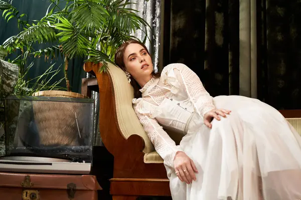 Una joven con un hermoso vestido vintage se relaja con gracia en un elegante espacio interior. - foto de stock