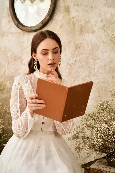 Una graziosa giovane donna legge un libro d'epoca in un ambiente sereno e rustico ornato di fiori. — Foto stock