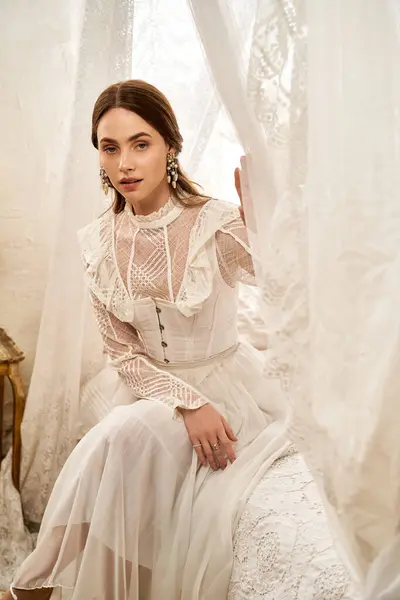 A beautiful young woman sits gracefully, draped in a vintage gown, surrounded by delicate fabrics. — Stock Photo
