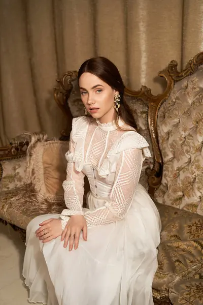 A beautiful young woman in a vintage dress exudes elegance while seated in a classic setting. — Stock Photo
