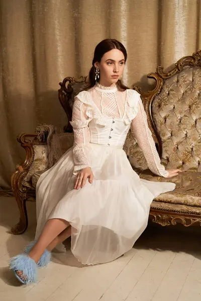 Uma jovem adorável em um vestido delicado se senta elegantemente em móveis ornamentados, exalando charme. — Fotografia de Stock