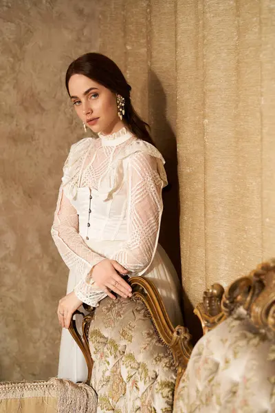 Young woman in a vintage dress leans gracefully against an ornate chair, exuding elegance. — Stock Photo