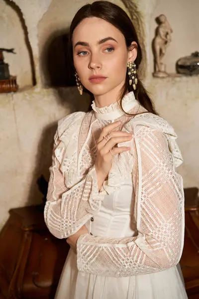 A beautiful young woman in a vintage dress stands gracefully in a rustic interior filled with charm. — Stock Photo