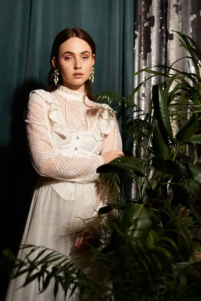 A graceful young woman in a vintage dress stands by vibrant plants, radiating elegance. — Stock Photo