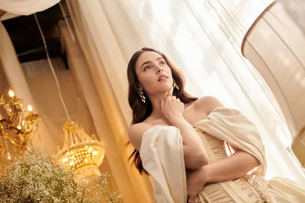 A lovely woman in a vintage dress poses gracefully under elegant chandeliers and soft light. — Stock Photo