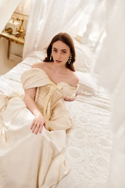 A graceful young woman in a vintage dress reclines elegantly on a soft bed, radiating charm. — Stock Photo