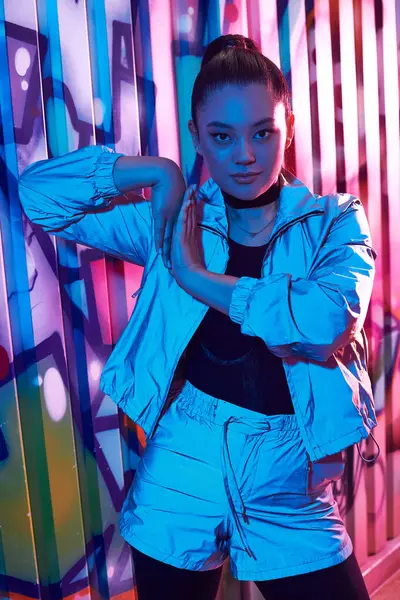 Confident woman showcases modern fashion against colorful graffiti in an urban night setting. — Stock Photo