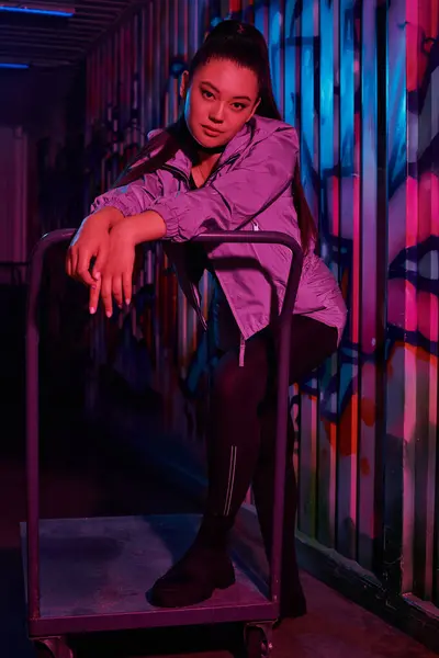 Stylish woman showcases her unique fashion sense against a colorful backdrop in a city corridor. — Stock Photo