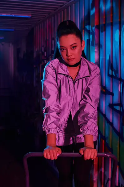 Une femme confiante pose dans une tenue élégante, éclairée par des lumières colorées et des graffitis. — Photo de stock